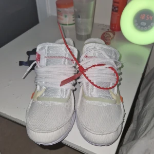 Nike x Off-White Presto vita sneakers - Oanvända Nike x Off-White Presto sneakers i vitt med mesh-överdel, tydliga Off-White detaljer som röd zip-tie och text på hälen. Kommer med extra skosnören i orange, svart och grönt. Snygg chunky sula och cool design som sticker ut.