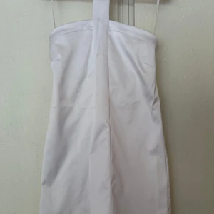 Vit axelbandslös klänning Topshop - Snygg vit axelbandslös klänning från Topshop med halterneck. Klänningen har en stilren, rak passform och är tillverkad i glansig polyester med lite stretch. Perfekt för dig som vill sticka ut med en minimalistisk look. Perfekt för midsommar, student eller andra festliga tillfällen.