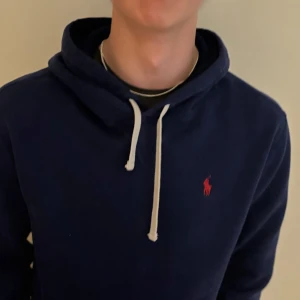 Mörkblå hoodie från Ralph Lauren - Snygg mörkblå hoodie från Ralph Lauren med vit snörning och klassisk röd logga på bröstet. Tröjan har huva och långa ärmar, perfekt för en chill och stilren look. Passar dig som gillar enkel men stilren look. Storlek S. Pris går att diskuteras 