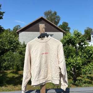 Beige sweatshirt från Carin Wester - Beige sweatshirt från Carin Wester med liten röd broderad logga på bröstet. Tröjan har rund hals, ribbade muddar och är i mjuk bomullsmix. 