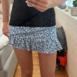 Blå blommig volangkjol - Supersöt kort blå kjol med vitt blommönster och volangkant från shein. Kjolen har en lätt utsvängd form och sitter snyggt i midjan. Den är högmidjad men jag har dragit tröjan över💞köparen står för frakt!