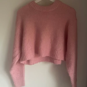 Rosa croppad stickad tröja H&M - Supermysig rosa stickad tröja från H&M med croppad passform och bred ribbad kant vid hals, ärmslut och nederkant. Perfekt för lager-på-lager och ger en chill vibe till din outfit.