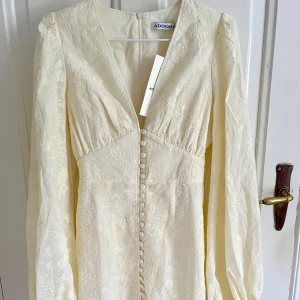 Adoore Florence dress light Yellow 34 - Superfin ljus spetsklänning från Adoore med v-ringning, långa puffärmar och knappar framtill. Inköpt för några veckor sedan, men endast provad så därför är prislapparna kvar! Kan skicka den omgående så den hinner fram till midsommar!💛