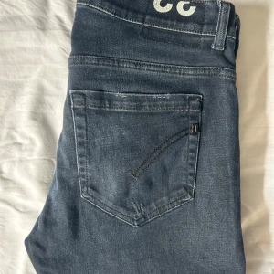 Dondup George Jeans Mörkblå - Snygga mörkblå jeans från Dondup i storlek 33 men passar 31-32. Jeansen har slim/skinny passform och snygga slitningar framtill. Klassisk femficksmodell med dragkedjegylf och vita logodetaljer bak i midjan. Inga defekter/skador!✌️