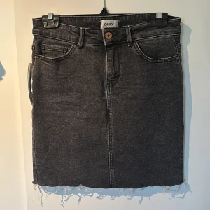 Jeanskjol - Svart jeanskjol från ONLY med rå kant nertill och klassiska femficksdetaljer. Kjolen är lång men går enkelt att sy upp! Fraktkostnad står köparen för.