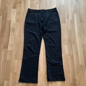 Svarta Fendi byxor med logomönster - Svarta byxor från Fendi med diskret, upphöjt logomönster över hela tyget. Klassisk rak passform och midja med knapp och dragkedja. Snyggt material med exklusiv känsla, perfekt för dig som gillar statement-plagg med lyxig touch.