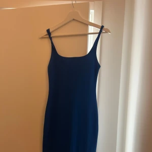 Blå tight klänning med smala axelband - En stilren blå klänning med smala axelband och rak, tight passform. Klänningen är marinblå och har en enkel, minimalistisk design utan mönster eller detaljer. Perfekt för dig som gillar en clean och klassisk look. Aldrig använd och i perfekt skick.