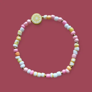 Färgglatt pärlarmband med citron - Sött armband med små pärlor i rosa, vitt, gult och guld. Armbandet har en rund pärla med citronmotiv.