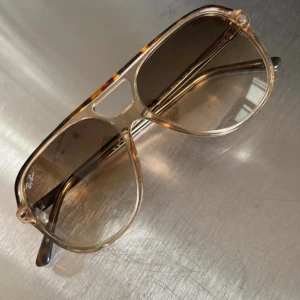 Ray-ban Bill  - Snygga Ray-Ban solglasögon med klassisk pilotform och transparent brun plastbåge. Glasen är bruna med lätt toning och bågarna har en diskret sköldpaddsmönstrad detalj upptill. Kommer med original Ray-Ban-fodral. 56 