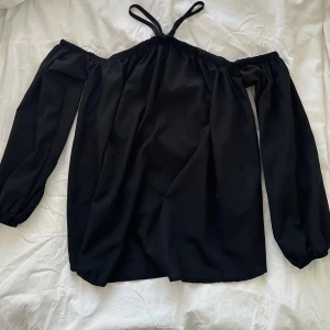 Svart top med bara axlar - Snygg svart off-shoulder blus med långa ärmar och smala band vid halsringningen. Blusen har resår vid axlarna för bästa passform. Storlek M. Mycket gott skick!!  Hämtas i Stockholm eller skickas mot porto. 