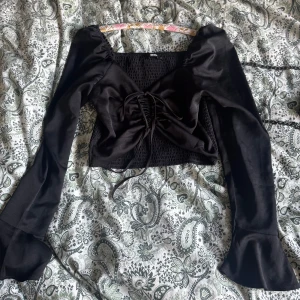 Svart topp med snörning - Supersnygg svart topp från Bikbok med armar som svänger ut vid händerna. Snörning.