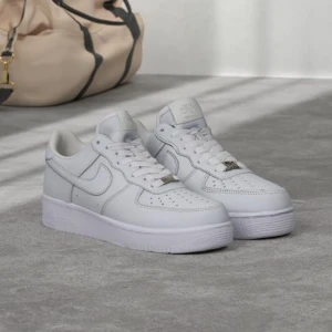 Nike Air Force 1 vita sneakers - Klassiska Nike Air Force 1 sneakers i helvitt skinn med lågt skaft. Snygg och clean design med perforerad tå, snörning och ikonisk Nike swoosh på sidorna. Perfekta för dig som gillar stilrena och tidlösa sneakers.kommer samt med rope snören ifall man vill ha 