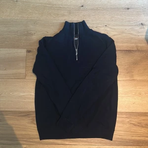 Mörkblå half zip tröja Ivanhoe M - Mörkblå långärmad tröja från Ivanhoe of Sweden med hög krage och half zip-dragkedja. Tröjan är stickad med merinoull och har en vindbrytande lager under tröjan, vilket gör den perfekt för kyliga dagar och passar dig som gillar stilren och funktionell design.