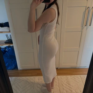 Vit ribbad ärmlös midiklänning - Supersnygg vit ribbad klänning med tight passform och ärmlös design. Klänningen har en rund halsringning och går ner till vaden, vilket ger en stilren och modern look. Perfekt för dig som gillar minimalistisk stil och vill ha något som framhäver figuren.