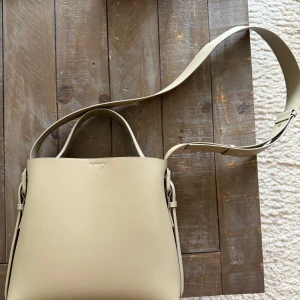 Beige/geön axelväska i skinnlook - Stilren beige/grön/khaki axelväska med minimalistisk design och slät yta. Väskan har både handtag och justerbar axelrem, samt magnetlås och ett rymligt huvudfack med innerficka. Perfekt för dig som gillar enkel och clean stil.