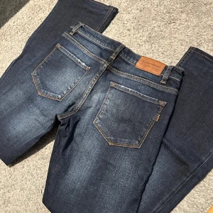 Mörkblå jeans från Peak Performance - Snygga mörkblå jeans från Peak Performance med klassisk femficksdesign och kontrastsömmar. Jeansen har en rak passform och är tillverkade i slitstarkt denim med lätt tvättade detaljer. Innerbenslängd: 72 cm. Midja - se bild. Storlek ca 27 eller 28.