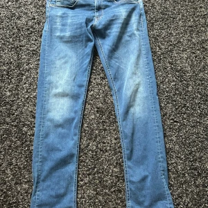 Replay Hyperflex Grover jeans blå - Säljer ett par Replay Hyperflex Grover jeans i klassisk blå tvätt. Jeansen har normal passform, raka ben och är tillverkade i stretchigt jeansmaterial för extra komfort. Snygga kontrastsömmar och klassisk femficksdesign. Perfekta för en avslappnad stil.