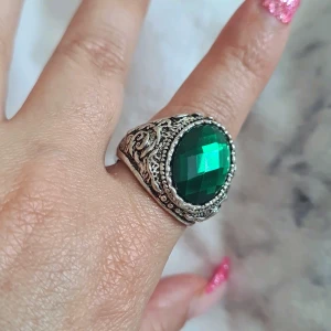 Vintageinspirerad silverring med grön sten - Helt ny Cool statementring i silverfärgad metall med en stor, facettslipad grön sten i mitten. Ringen har snygga, detaljerade mönster längs sidorna som ger en vintagevibe. Perfekt för dig som vill sticka ut med accessoarer!
