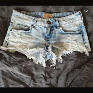 Ljusblå slitna jeansshorts Bershka - Snygga ljusblå jeansshorts från Bershka med slitna detaljer och fransig kant. Klassisk femficksmodell med låg midja och knappstängning. Perfekta för sommaren när du vill ha en avslappnad och trendig look.