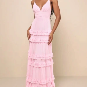 Ljusrosa långklänning med volanger - Supersöt ljusrosa långklänning från Lulus med djup v-ringning, smala axelband och flera lager volanger. Klänningen har en flowy passform och är perfekt för sommarens alla tillfällen. Säljer då den var för liten och missade retur datumet. På bild 3 är en bild hur den sitter på i storlek XS vilket inte är den jag säljer, den som jag säljer är i storlek XXS. Kommer postas i ordinarie paketet som ses på bild 4, pris lapp och allt fins kvar på kläningen! Nypris och köpt för 1300kr från lulus hemsida.