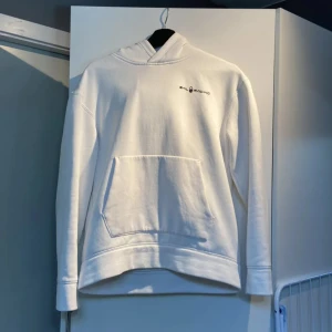 Vit hoodie från Sail Racing - Vit hoodie från Sail Racing med diskret logga på bröstet och en större logga på huvan. Klassisk känguruficka framtill och mjuk insida. Perfekt för dig som gillar stilren och enkel design. Långärmad och med huva för extra komfort.