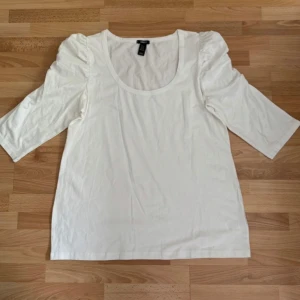 Ny. Vit topp med puffärm från H&M, XL - Säljer en vit topp från H&M i storlek XL. Toppen har puffade axlar och trekvartsärm, rund halsringning och är gjord i mjuk bomull. Perfekt för dig som gillar en enkel men trendig look med lite extra volym på ärmarna.