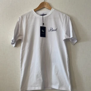 Vit t-shirt Leon Marcél med tryck XS - Vit t-shirt från Leon Marcél i bomull, med korta ärmar och rund hals. Framsidan har en stilren logga och baksidan ett stort blått tryck med vinflaska, glas och båt. Perfekt för dig som gillar snygga detaljer och unik design.