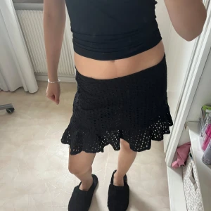 Svart volangkjol med broderade hål - Supersöt svart kortkjol med volangkant och broderade hål i hela tyget. Kjolen är från bohoo och passar xs-s