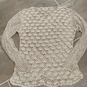 Silvrig virkad tröja från Small Talk - Superfin beige virkad tröja från Small Talk i storlek L. Tröjan har lång ärm, v-ringning och ett detaljerat spetsliknande mönster över hela plagget. Perfekt för lager-på-lager och ger en chill men ändå snygg vibe.