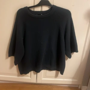 Svart stickad tröja från 157 - En svart stickad tröja från 157 med rund halsringning och avslappnad passform. Tröjan har trekvartsärmar och är perfekt för lager-på-lager-stil. Enkel och stilren design som funkar till många olika outfits.