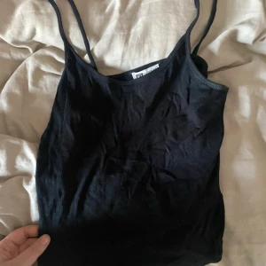 Svart ribbad linnetopp FB Sister - En svart ribbad linnetopp från FB Sister i storlek M. Toppen har smala axelband och är tillverkad i ett mjukt, stretchigt material som sitter snyggt på kroppen. Perfekt att styla med jeans eller kjol för en enkel och clean look.