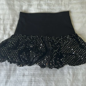 Svart paljettkjol från Zara - Supersnygg svart kortkjol från Zara med glittriga paljetter på volangdelen. Kjolen har en tight, stretchig midja och en festlig look som verkligen sticker ut. Jag är 155 cm så det passar om man är längre än 140cm🤗