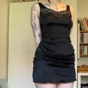 Svart bodycon klänning / underklänning med spets  - Snygg svart klänning med  v-ringning dekorerad med spets. Klänningen har en figurnära passform och är tillverkad i ett glansigt material som ger en cool look. Perfekt för dig som gillar en stilren men edgy vibe. Tror den är avsedd som underklänning, men funkar lika bra att ha den bara som den är! Slutar vid knäna på mig som är 170cm lång, men går även att dra upp den (som på första bilden) och ha som kortare klänning✨