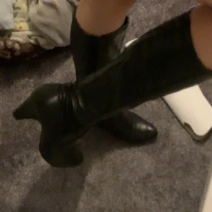 Svarta stövletter med klack - Snygga svarta stövletter med spetsig tå och smal klack. Skorna är höga och går upp till vaden, tillverkade i ett material som ser ut som skinn. Perfekta för dig som vill ha en edgy och stilren look.