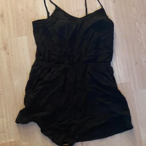 Svart kort klänning med smala axelband - En svart kort klänning med smala axelband och v-ringad hals. Modellen är enkel och luftig, perfekt för varma dagar. Midjan är lätt markerad för en snygg siluett. Passar dig som gillar minimalistisk stil.