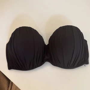 Bandeaubikini - Jättefin svart bandeau bikinitopp från Dorina med  rynkade kupor och stadig passform och bygel. Toppen har en stilren look utan axelband och stängs med spänne bak. Liten silikonremsa längs båda sidorna för att den ska hållas upp enklare. Fraktkostnad står köparen för:))