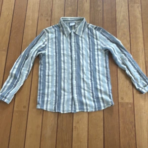 Randig skjorta Knowledge Cotton Apparel - Snygg randig skjorta från Knowledge Cotton Apparel i blått och beige. Skjortan har klassisk krage, knäppning framtill och långa ärmar. Tillverkad i mjuk bomull, perfekt för en chill och stilren look.