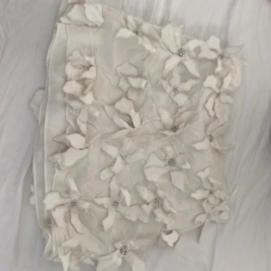 Vit blommig minikjol från Zara - Superfin vit kortkjol från Zara med 3D-blommor och pärldetaljer. Kjolen har en unik design med blommor över hela tyget och är perfekt för en utekväll. Materialet känns lätt och somrigt, och kjolen har en snygg passform som framhäver benen. Använd ENDAST en gång så i helt nyskick 