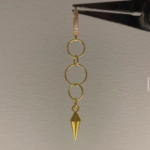 Guldigt örhänge med ringar och spets - Coolt örhänge i guld med tre sammankopplade ringar och en spetsig hängande detalj längst ner. Översta delen har små glittrande stenar för extra bling. Perfekt för dig som gillar statement-smycken med edgy vibe.