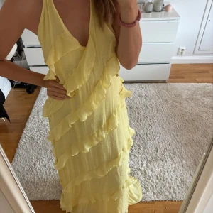 Gul långklänning med volanger - Superfin ljusgul långklänning med djup v-ringning och volangdetaljer över hela klänningen. Klänningen är ärmlös och har öppen rygg, perfekt för sommarens alla tillfällen. Materialet känns lätt och luftigt. Finns ingen lapp så skulle uppskatta storleken till en S/M då den är lite för stor för mig som vanligtvis har XS. Finns en fläck på ena bandet som syns på sista bilden💛