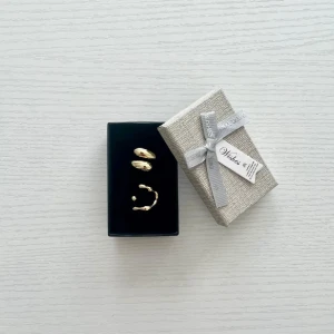 Extra ring på köpet  - Säljer ett par trendiga guldiga ringar med cool, organisk och oregelbunden form. Kommer i en snygg presentask med rosett, perfekt som present till någon du gillar eller till dig själv.