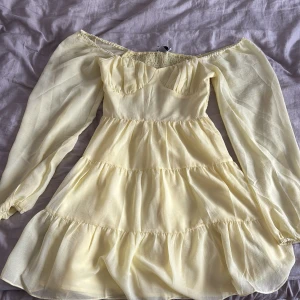 Ljusgul offshoulder volangklänning - Superfin ljusgul kortklänning med offshoulder och långa, luftiga ärmar. Klänningen har flera volanglager och smock i ryggen för en bekväm passform. Det är jätteskönt material på klänningen och perfekt för sommaren. Fin gul färg också😍Använd en gång men har en minimal fläck på sig (kolla sista bild)