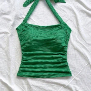 Grön ribbad linnetopp - Snygg grön halterneck topp med knyt i nacken. Toppen har en vågig mönster typ i tyget, den är lite stretch i men inte jättemycket. Jag tror de. är från vero moda.