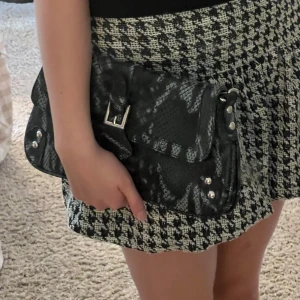 Handväska ormskinn - Snygg svart handväska i syntetmaterial med ormskinnsmönster. Väskan har en kedja som axelrem och en praktisk dragkedja inuti. Den är i mycket bra skick och har inga defekter!