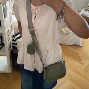 Söt väska - Söt väska med en liten mini väska till, perfekt att ha tex AirPods i eller kontanter! Har nån liten fläck där man stänger men när man stänger väskan så syns den inte! Man kan även ta av banden och mini väskan om man inte alltid vill ha det på!