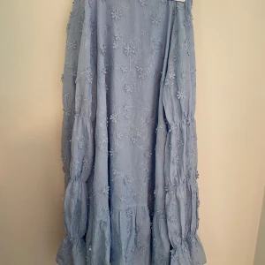 Ljusblå blommig långklänning - Superfin ljusblå klänning med broderade blommor och volangdetaljer. Klänningen har långa ärmar och en snygg öppen rygg🩷
