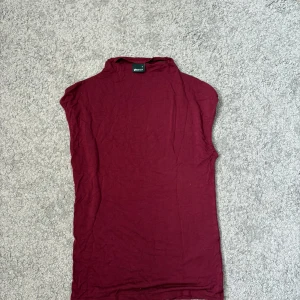 Vinröd polotopp från Gina Tricot - Snygg vinröd polotopp från Gina Tricot i mjuk bomull. Toppen är ärmlös med hög krage. Stretchigt material. Knappt använd. Pris kan diskuteras. 