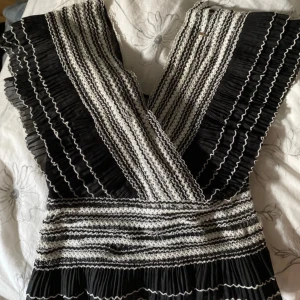 Svartvit randig omlottblus  - Supersnygg kort omlottklänning från By Malina i svart och vitt med randigt mönster och volangdetaljer. Djup v-ringning och plisserade partier ger en unik look. Perfekt för dig som vill sticka ut med en cool och trendig stil.