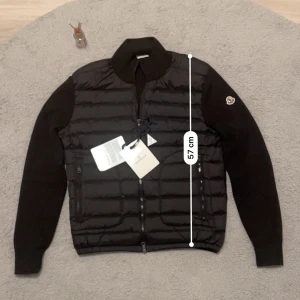 Svart pufferjacka från Moncler - Snygg svart pufferjacka från Moncler med quiltad front och ärmar i stickad ull. Jackan har dragkedja framtill, två sidofickor med dragkedja och Moncler-logga på ena ärmen. Perfekt för dig som vill ha en stilren och exklusiv look.Jag är 181 och den passar mig perfekt. Den är i storlek M men kan passa S också, se även mått.Den är helt ny och äkta, Scan funkar allt. Perfekt till hösten 🍂  och vintern 🥶 Aktiv 24/7✅ Skickas inom 24h📦🚚 Kan gå ner i hugget 😃✅ Hör av er via frågor⁉️