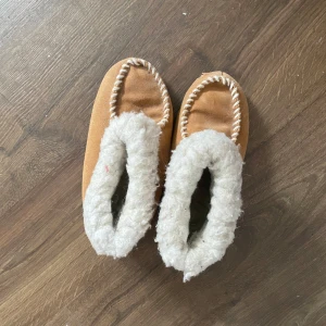 Tofflor med ullfoder - Mysiga tofflor  med vitt, fluffigt fejk ullfoder och dekorativa sömmar runt öppningen. Perfekta för kalla dagar när du vill hålla fötterna varma och sköna hemma. Klassisk design med platt sula och rund tå. Dem är lite smutsiga på undersidan men inget som man tänker på 🌸